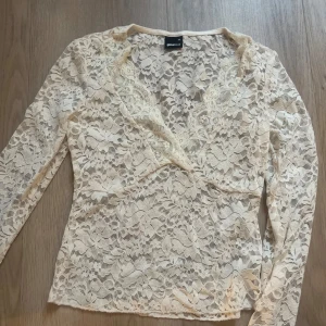 Beige spetsblus från Gina Tricot - Supersnygg beige spetsblus från Gina Tricot i storlek XS. Blusen har lång ärm, v-ringning och är helt täckt av blommig spets. Perfekt för dig som gillar romantiska detaljer och vill sticka ut lite extra.