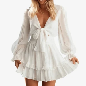 Vit omlottklänning med volanger - Supersöt vit studentklänning med omlott och knyt framtill. Klänningen har långa, lätt puffade ärmar och volangdetaljer på kjolen. Tillverkad i ett lätt och luftigt material som ger en flowy känsla. Perfekt för dig som gillar romantisk och trendig stil. Funkar även perfekt till konfirmation!                                                 