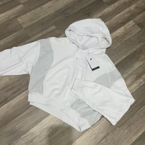 Vit hoodie Nike Air croppad  - Snygg vit croppad hoodie från Nike Air med huva och diskret logga framtill. Tröjan har långa ärmar och bred mudd nertill. Tillverkad i mjuk bomullsblandning, perfekt för en sportig och avslappnad look. Köpt för 950 kr