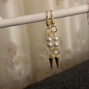 Guldiga örhängen med pärlor och spikes - Unika örhängen med guldfärgade ringar, fyra vita pärlor i mitten och coola guldiga spikes längst ner. Perfekt accessoar för dig som vill sticka ut med en edgy men ändå elegant stil.