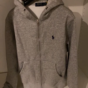 Grå Ralph Lauren kofta  - Grå kofta från Polo Ralph Lauren med dragkedja. Jag säljer den då jag inte använt den så ofta. Den är storlek M men passar nog bäst för storlek S.