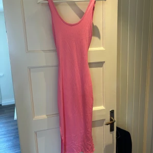 Rosa ribbad långklänning med öppen rygg - Säljer en snygg rosa långklänning i ribbat material. Klänningen är ärmlös med smala axelband och har en cool twistad detalj och öppen rygg. 