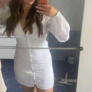 Broderad vit studentklänning - Superfin vit kort klänning från NA-KD med broderade blommor, v-ringning och långa ärmar. Klänningen har knappar framtill och är den absolut finaste studentklänningen jag någonsin sätt🥺Klänning säljs inte längre, så du kommer troligen va ensam med att ha den😆💓😘 Prova att buda!🙌🏼