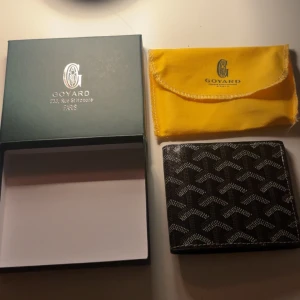 Svart  plånbok med mönster - Säljer en svart  plånbok i skinn med ikoniskt grafiskt mönster i vitt och grått. Plånboken har flera kortfack och levereras med original ask och gul dustbag. Perfekt för dig som vill ha en lyxig och stilren accessoar.