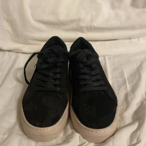 Svarta sneakers från Vagabond - Svarta sneakers från Vagabond med ovandel i mocka och klassisk snörning. Skorna har en chunky, beige platt sula som ger en modern vibe. Perfekta för dig som gillar stilrena och trendiga skor med en clean look.