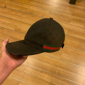 Keps med grön och röd rand - Snygg svart keps  med diskret rutmönster och klassisk grön-röd rand på sidan. Kepsen har böjd skärm och justerbar rem baktill. Perfekt accessoar för en trendig streetstyle-look. Solblek men i gott skick