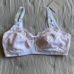 Oanvänd Vit spetsig bh från Amoena - Säljer en vit bh från Amoena, modell Karolina SB. Den har tunna axelband, vackra spetsdetaljer och diskreta ränder på kuporna. Framtill sitter en liten rosett. Materialet är mjukt och bekvämt. Skulle säga att den är en storlek mindre i kupa🫶🏻