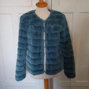 Blå pälsjacka från Vero Moda - Säljer en fluffig blå pälsjacka från Vero Moda i storlek M. Jackan har lång ärm, rund halsringning och är sydd i breda, horisontella paneler för en cool look. Perfekt för dig som vill sticka ut med en mjuk och trendig jacka.