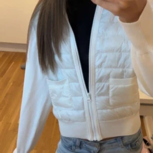 Vit quiltad kofta från Gina Tricot - Säljer en vit quiltad kofta från Gina Tricot med dragkedja framtill och två fickor. Koftan har ribbade muddar och är i en croppad modell. Perfekt att slänga på sig över en t-shirt eller topp för en fräsch look.