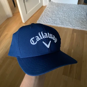 Mörkblå Callaway keps Odyssey - Snygg mörkblå keps från Callaway med broderad logga framtill och Odyssey-detalj bak. Justerbar rem baktill och tillverkad i 100% polyester. Perfekt för golfbanan eller som cool accessoar till vardags. Kepsen är helt ny men säljer den då den inte passar på mitt huvud.