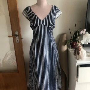 Randig långklänning med spetsdetalj💕 - Säljer en långklänning med marinblå och vita vertikala ränder. Klänningen har v-ringad hals och är ärmlös med spetsdetalj vid axlarna. Passformen är normal och tyget känns som bomull. Perfekt för dig som gillar retrovibbar och snygga mönster.💕