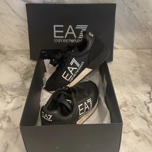 Svarta sneakers från Emporio Armani EA7 - Snygga svarta sneakers från Emporio Armani EA7 med tydlig logga på sidan. Perfekta för en sportig och trendig look. Äkta köpta i varuhus i Nice. 