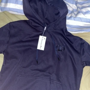 Mörkblå CD hoodie - Säljer en snygg mörkblå hoodie från CD med broderad CD-logga på bröstet. Tröjan har huva med snörning och en klassisk magficka. Perfekt för dig som vill ha en stilren och exklusiv look. Helt oanvänd och priset kan diskuteras vid snabbaffär.