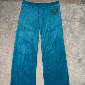 Vintage Juicy Couture velour byxor - Turkosa mjukisbyxor från Juicy Couture i glansig velour med krona framtill. Byxorna har normal passform, raka ben och dragsko i midjan. 