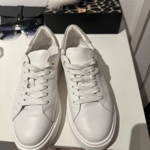 Vita sneakers från D.A.S.I.A med platåsula - Snygga vita sneakers från D.A.S.I.A med chunky platåsula och snörning. Ovandel i vitt skinn och detaljer i beige mocka vid hälen. Guldiga metalldetaljer vid snörning! Skickar mer bilder vid intresse 🙂