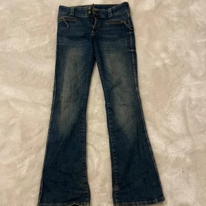 Low waist Blå bootcut jeans från H&M - Skit Snygga blå bootcut jeans från H&M med låg midja och justerbar midja. Jeansen har dragkedjor på fickorna framtill och klassisk denimlook med lätt slitning.De är lite slits vid slutet av byxan man man ser de knappast annars i ett bra skick
