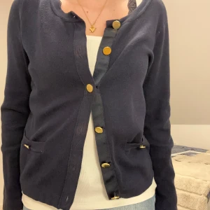 Mörkblå kofta från Stockh LM med guldknappar - Snygg mörkblå kofta från Stockh LM med rund halsringning och guldiga knappar framtill. Koftan har två små fickor framtill och är långärmad. Perfekt till hösten! Säljer en rosa och svart också! 