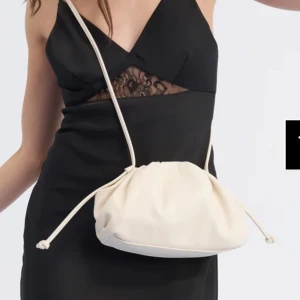 Vit axelväska med snörning - Snygg vit axelväska med cool snörning och mjuk, rundad form. Perfekt storlek för mobilen och det viktigaste. Väskan har en minimalistisk look och är tillverkad i skinnliknande material. Enkel att slänga över axeln för en trendig vibe.