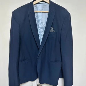 Mörkblå kavaj från ASOS - Snygg mörkblå kavaj från ASOS med klassisk passform och ljusblått foder. Kavajen har smala slag, tre fickor framtill och en innerficka med knapp. Perfekt för dig som vill ha en stilren och enkel look.