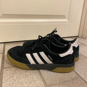Adidas Spezial svarta sneakers - Svarta Adidas Spezial sneakers i mocka med klassiska vita ränder och vit hälkappa med Adidas-logga. Skorna har snörning och en brun gummisula. Synligt använda.