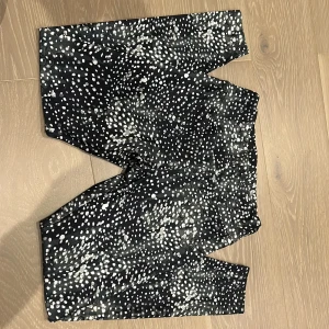 Svarta leggings med vitt prickigt mönster - Snygga svarta leggings med vitt prickigt mönster som ger en cool och unik look. Perfekta för dig som vill sticka ut och ha något bekvämt men ändå trendigt. Stretchigt material som sitter skönt och följer kroppen.