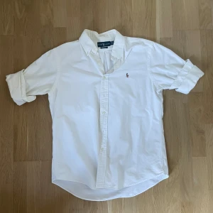 Vit skjorta från Ralph Lauren L - Klassisk vit skjorta från Ralph Lauren i bomull med button-down krage och broderad logga på bröstet. Custom fit-modell med långa ärmar och knappar framtill. Perfekt för en clean och stilren look.