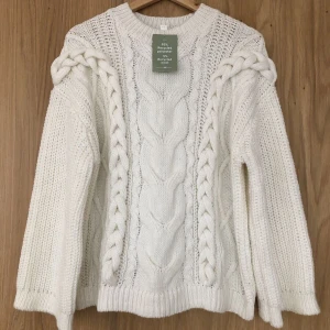 Vit oversized kabelstickad tröja - Supermysig vit stickad tröja med grova flätor längs ärmar och fram, oversized passform och rund halsringning. Tröjan är gjord i en blandning av återvunnen polyester och ull, perfekt för kyliga dagar. Snygg att styla med jeans eller kjol för en trendig look🤍 storlek S, från H&M. Använd men i mycket bra skick!