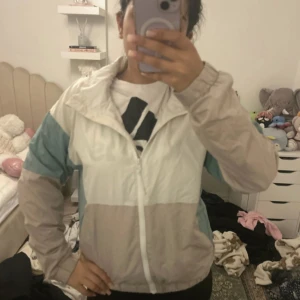 vindjacka från McKinley - Säljer en snygg vindjacka från McKinley i färgblock med beige, vitt och ljusblått. Jackan har dragkedja framtill, huva och långa ärmar. Perfekt för blåsiga dagar och enkel att matcha med olika outfits.