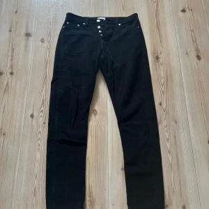 Svarta manchesterbyxor från Samsøe Samsøe 30/32 - Svarta manchesterbyxor från Samsøe Samsøe med raka ben och klassisk femficksmodell. Byxorna har silverfärgade knappar framtill och ett snyggt läderpatch med logga bak i midjan. Perfekta för dig som gillar stilrena och tidlösa plagg.