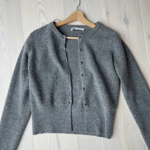 Grå kofta från Zara med knappar - Mysig grå kofta från Zara i stickat material. Koftan har rund halsringning, långa ärmar och snygga silvriga knappar framtill. Perfekt att slänga över en t-shirt eller linne för en chill look💕