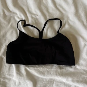 Svart linnetopp med smala axelband från soc  - En enkel och stilren svart linnetopp med smala axelband som korsas i ryggen. Sport-bh passar perfekt för träning. Materialet känns mjukt och stretchigt, vilket gör den bekväm!