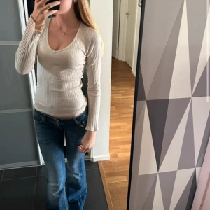 Beige ribbad långärmad tröja - Säljer en beige långärmad tröja med v-ringning och ribbad struktur. Tröjan är figurnära och har en enkel, stilren design som passar perfekt till jeans eller kjol. Superenkel att matcha och riktigt skön att ha på sig. Inga skador alls, knappt använd! 