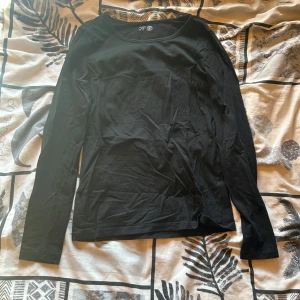 Svart långärmad bomullströja - En enkel och stilren svart långärmad tröja från Lindex. Tillverkad i mjuk bomull med rund halsringning och rak passform. Perfekt basplagg att ha i garderoben.