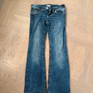 Blå bootcut jeans från Gina Tricot - Snygga blå jeans från Gina Tricot Young i bootcut-modell med klassiska fickor fram och bak. Jeansen har låg midja, bootcut leg och skön mjuk stretch. Knäppning med dragkedja och knapp.