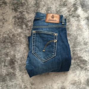 Blå  jeans från Dondup - Säljer ett par blå skinny  från Dondup med klassisk femficksdesign och snygga kontrastsömmar. Jeansen har läderpatch med logga bak i midjan och är tillverkade i ett mjukt denimtyg. 