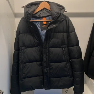 Svart pufferjacka från BOSS - Säljer en svart pufferjacka från BOSS. Nypris 3000 kr och endast använd en vinter säsong.