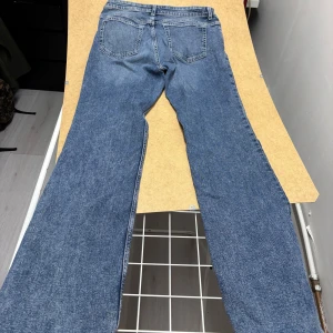 Blå lågmidjade jeans från H&M  - Snygga blå jeans från H&M Divided i straight leg-modell. Klassisk femficksdesign och normal passform. Jeansen är tillverkade i bomull och har en tidlös blå tvätt som passar till det mesta. Perfekta för dig som gillar en avslappnad och trendig look.