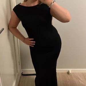 Svart långklänning med öppen rygg - En svart långklänning med tight passform och snygg öppen rygg. Klänningen har rynkade detaljer baktill som ger en cool effekt. Ärmlös design och mjukt, stretchigt material som sitter skönt på kroppen. Scrunchdetalj på rumpan som framhäver rumpan i klänningen, använd max 2 gånger. Lappen på klänningen är sönder därav priset🩵