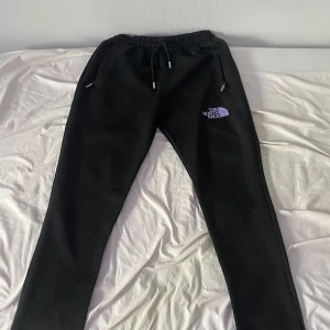 North Face byxor - svart - Svarta träningsbyxor från The North Face med vit logga på vänster ben. Byxorna har elastisk midja med snörning och raka ben. Perfekta för chill eller träning, med mjukt material och bekväm passform. Pris kan diskuteras men börjar på 400. Passar bäst dig som är ca 170–180 cm lång beroende på önskad passform. Byxorna är använda ett fåtal gånger.
