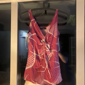 Röd mönstrad linnetopp Vero Moda - Säljer en snygg röd linnetopp från Vero Moda i storlek S. Toppen har ett vitt abstrakt mönster, v-ringning och en cool knytning framtill. Den är ärmlös och har en lätt, mjuk känsla som passar perfekt till varma dagar.