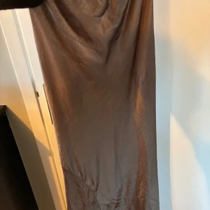Brun långkjol i satin - En stilren brun långkljol i glansigt satinmaterial. Kjolen har en rak och enkel siluett som faller snyggt längs kroppen. Perfekt för dig som gillar minimalistisk och elegant stil.