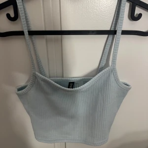 Ljusblå ribbad linnetopp H&M Divided - Supersöt ljusblå croppad linnetopp från H&M Divided. Toppen är ribbad med smala axelband och har en enkel, stilren design som är perfekt till jeans eller kjol. Mjuk och stretchig för en bekväm passform.