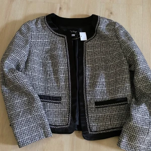 Rutig kavaj från Afound Rouge - Stilren rutig kavaj från Afound Rouge i svart och vitt. Jackan har rundad halsringning, svarta detaljer vid fickor och kanter samt lång ärm. Perfekt för en chic och trendig look.