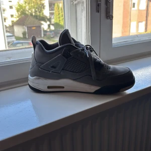 Nike Air Jordan 4 Retro Cool Grey - Säljer ett par Nike Air Jordan 4 Retro Cool Grey. Skorna är gråa med vita och svarta detaljer, meshpaneler på sidorna och silverfärgad Jumpman-logga på hälen. Klassisk siluett med snörning och platt sula. Ovandelen är i mocka och syntetmaterial.