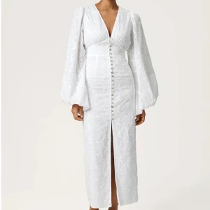 Vit Adoore klänning - Superfin vit Positano-klänning från Adoore med v-ringning, långa puffärmar och knappar framtill. Klänningen har broderade blommor i tyget och en lätt slits nedtill. Helt ny med prislapp.💕💕ny pris 1695