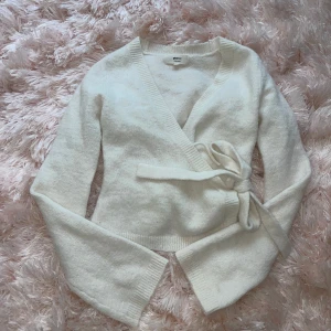  omlottkofta med knyt från Gina Tricot - Superfin  omlottkofta från Gina Tricot med knyt i sidan och v-ringad hals. Mjuk och skön stickad känsla, perfekt för lager på lager. Långärmad och ribbade muddar vid ärmslut och nederkant. Enkel att styla till olika outfits.