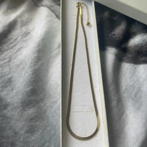 Guldigt kedjehalsband med hjärtdetalj / 18 k guldpläterad halsband - Säljer ett stilrent halsband i guldton med platt kedja och justerbar längd. Kedjan har en elegant, slät design och avslutas med en liten hjärtberlock vid låset. Köpt i Turkiet! Perfekt för att lyfta vilken outfit som helst.