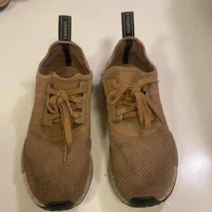 Adidas NMD sneakers i beige mesh - Säljer ett par Adidas NMD sneakers i snygg beige färg. Skorna har ovandel i ventilerande mesh, klassiska tre ränder på sidan och en boost-sula för extra komfort. De har snörning och svarta detaljer på sulan och hälen. Perfekta för dig som gillar streetwear och stilren design. Obs. skorna har fått litet slitage på vänster fot.