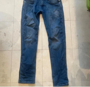 Replay Anbass slim fit jeans blå - Säljer ett par snygga Replay Anbass jeans i klassisk blå färg. Modellen är slim fit med raka ben och fem fickor. Jeansen har coola detaljer på bakfickorna och är tillverkade i mjukt jeansmaterial som sitter skönt hela dagen.