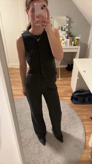 Randig kostymväst och byxa från MNG - Säljer en svart kostymväst och matchande byxa från Mango. Setet är ärmlöst och har smala vita ränder, knäppning framtill och fickdetaljer på västen. Byxorna är raka och har samma randiga mönster. Perfekt för dig som gillar en stilren och modern look! Säljes pga de kommer ej till användning. Ny utan prislapp.